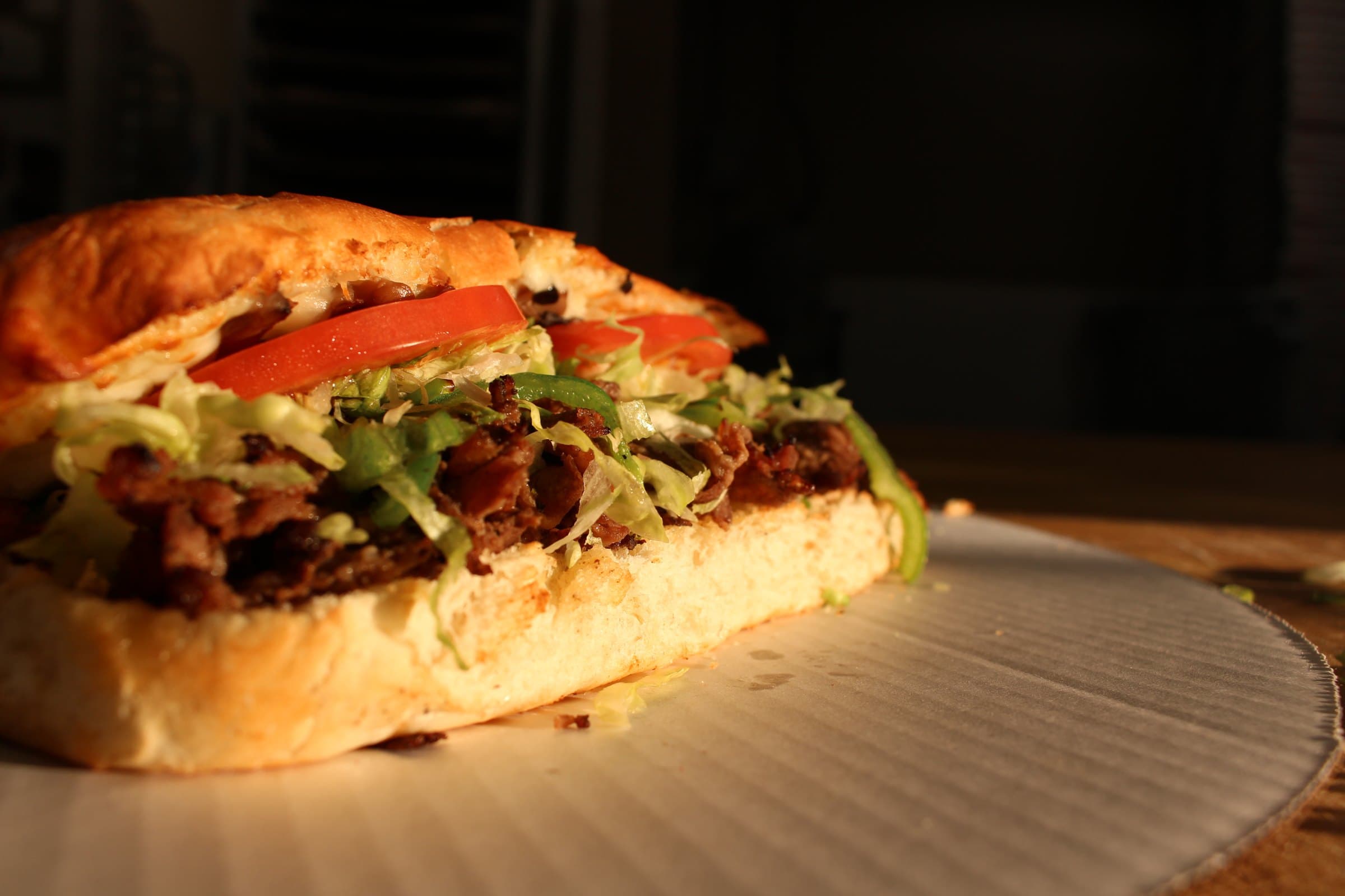 A steak grinder with peppers, lettuce, and tomato on a toasted roll.