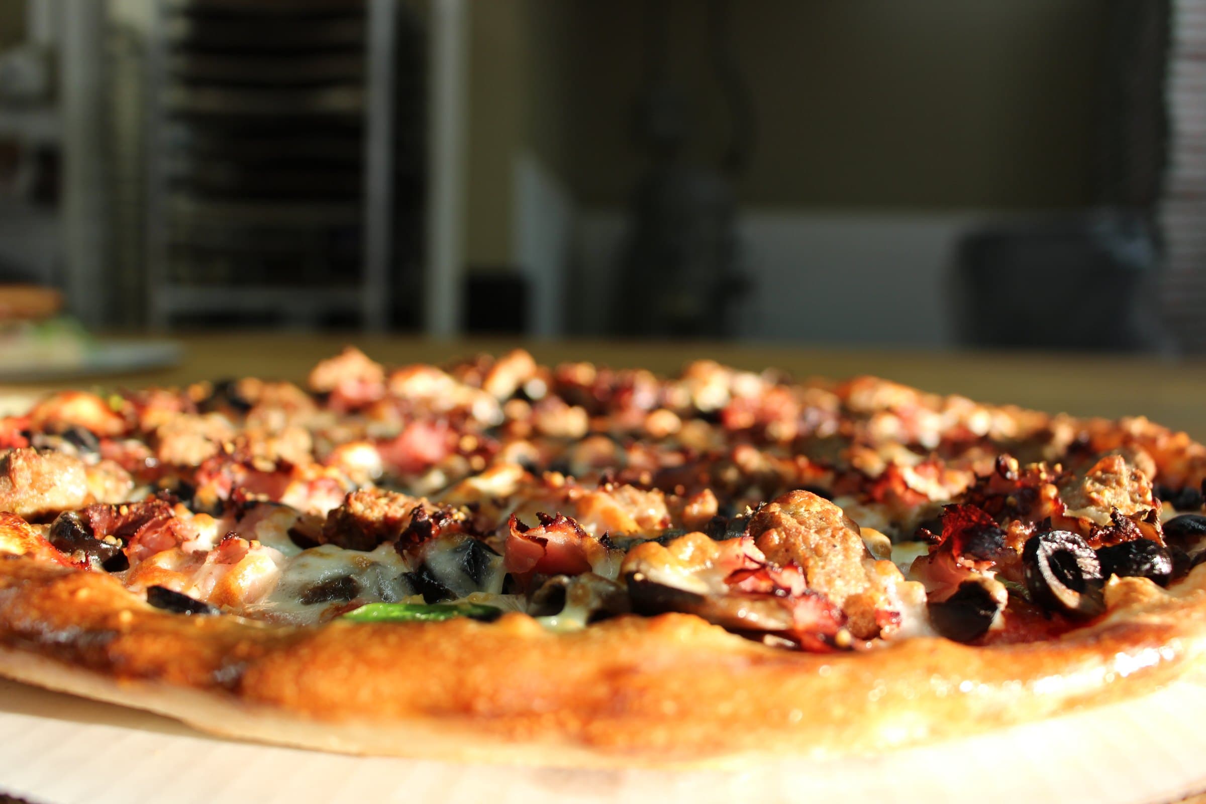 Close-up of a Mancino's pizza with a golden crust, melted cheese, sausage, ham, and olives.